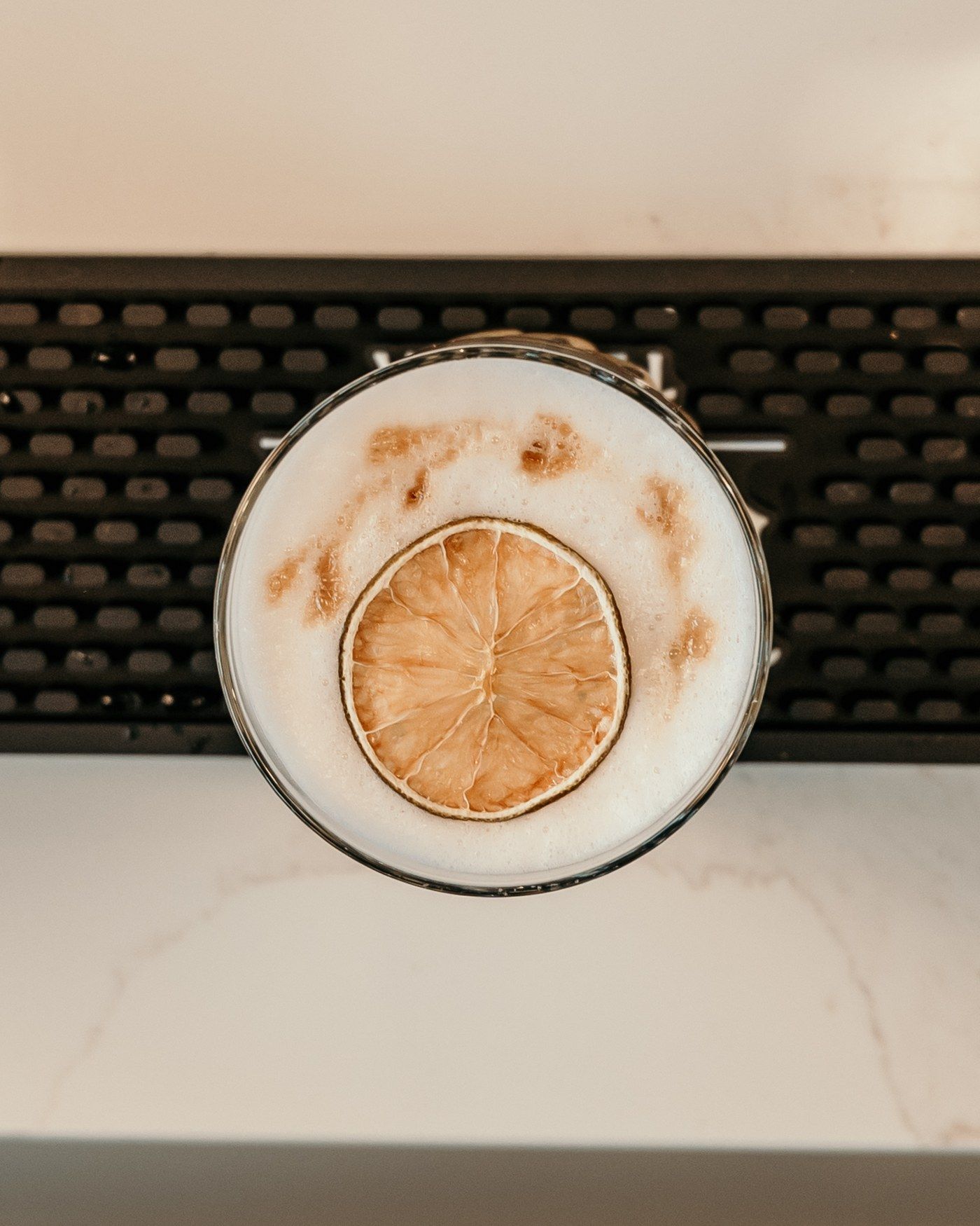 A foamy cocktail with a dried citrus wheel, seen from above on a bar mat