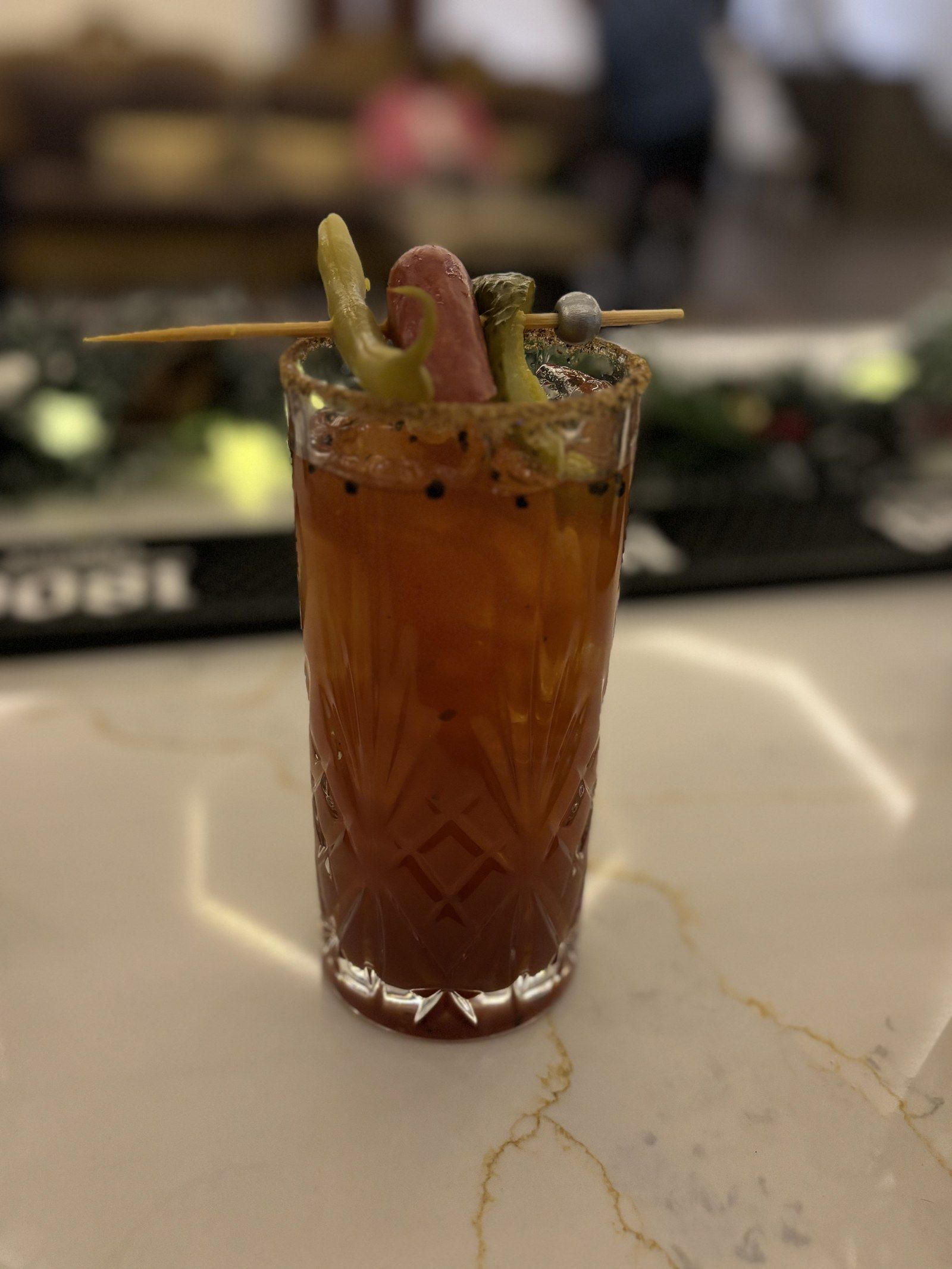 A Caesar with a spiced rim and a skewer of pickle, pepper and sausage