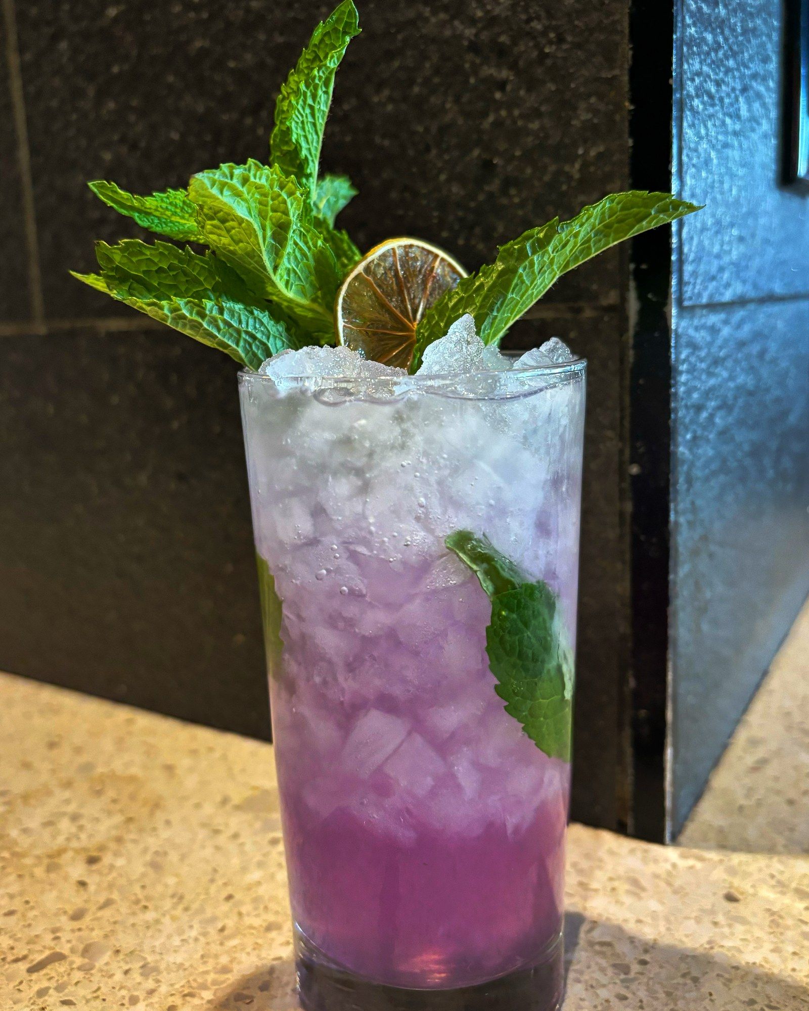 A purple highball over crushed ice with fresh mint and a dried lime wheel