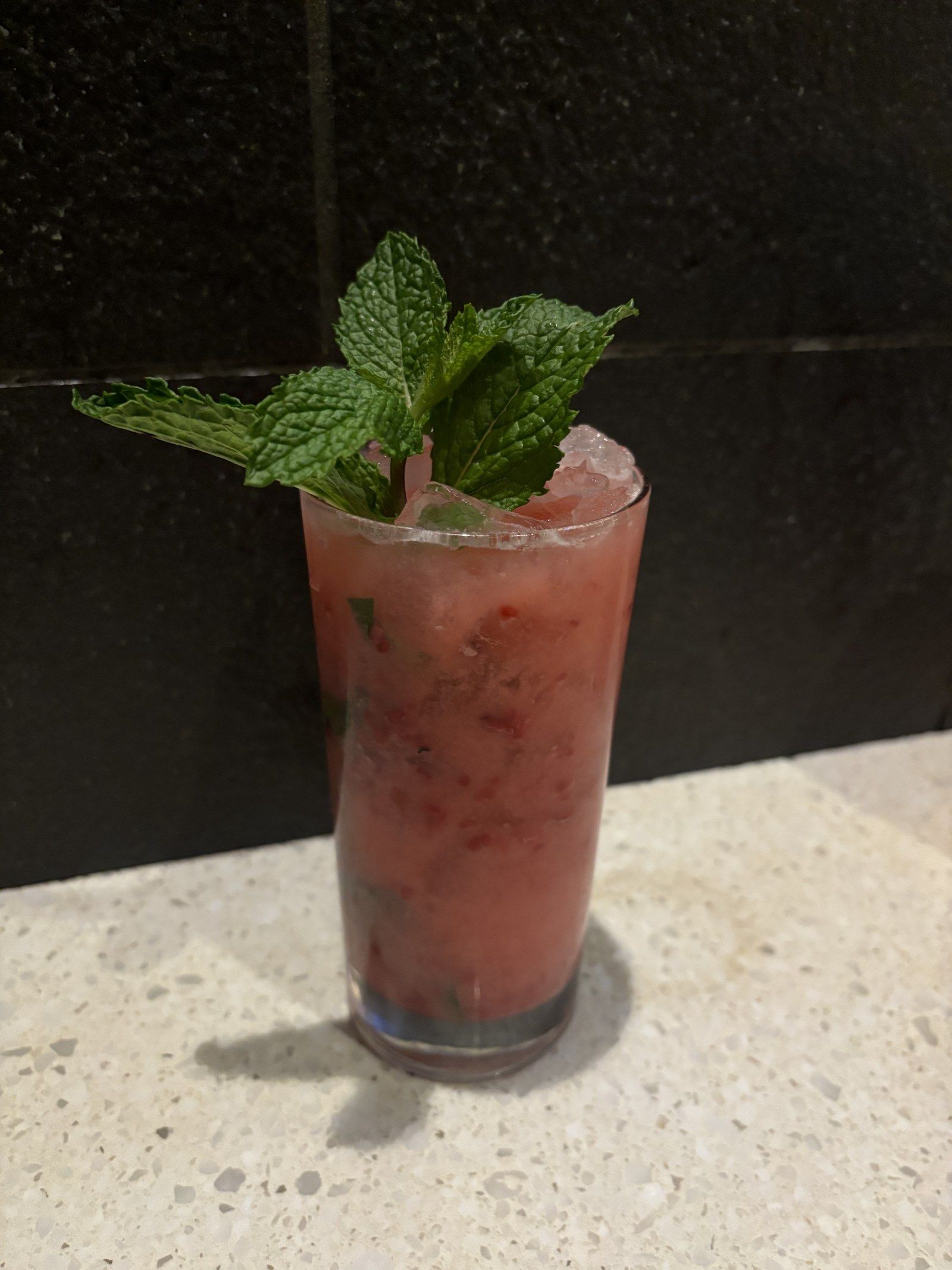 A raspberry red highball with muddled berries and a mint crown on a stone counter