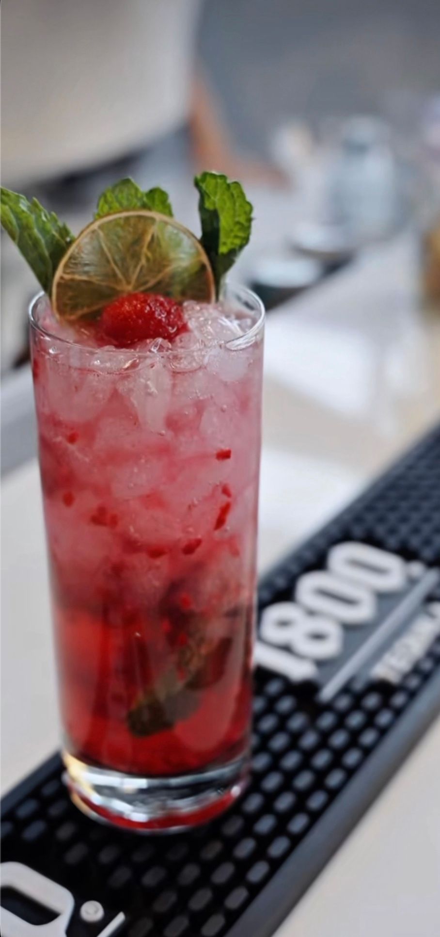 A tall muddled berry drink with mint and a dried lime wheel